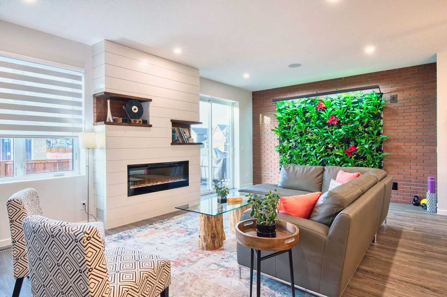 Beautiful living room with windows and patio sliding doors. A gas fireplace and living wall with green plants also featured in this beautiful net zero home.