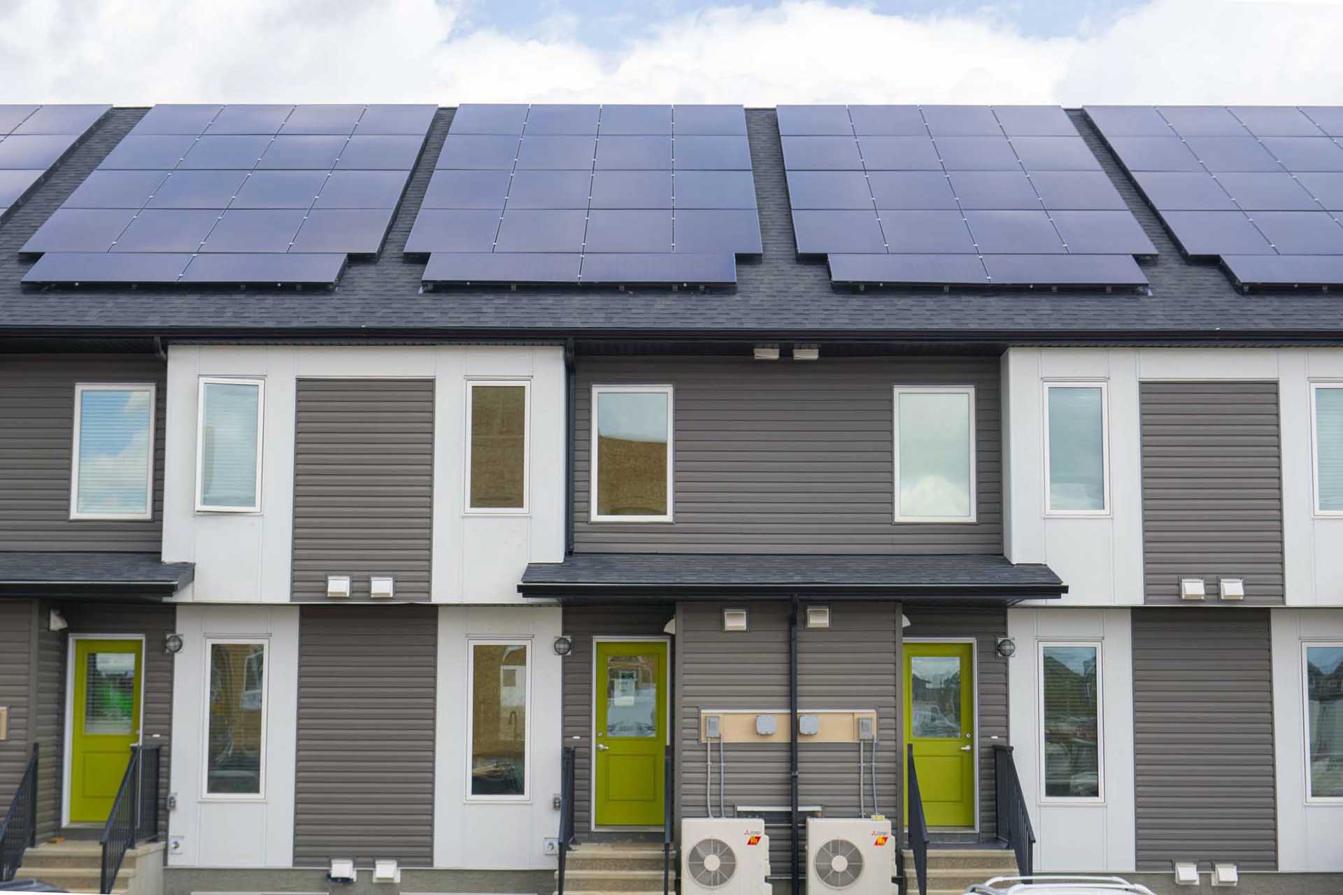 ZEN Sequel net zero building with a roof fully covered in solar panels and back doors of these townhomes in a brigh green colour