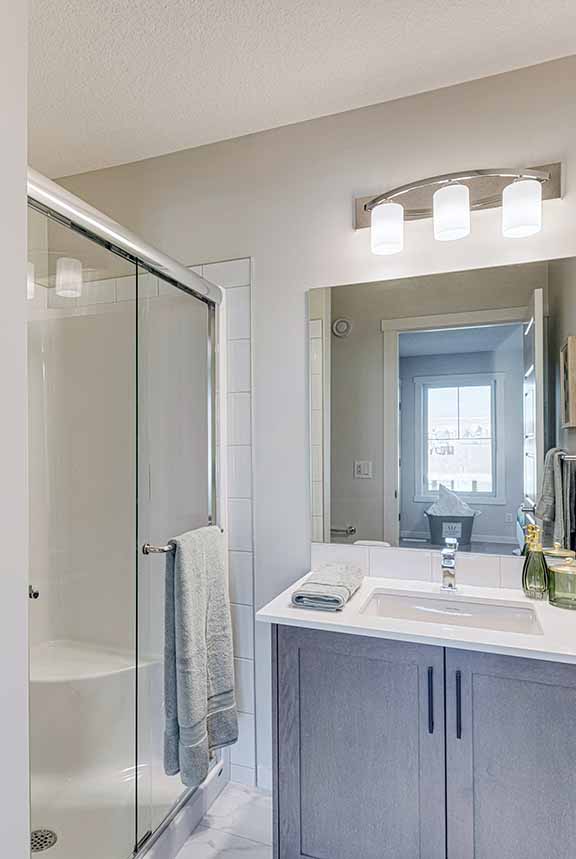 Ensuite bathroom of the ZEN Livingston showhome with large mirror, bright lights above and glass door walk-in shower