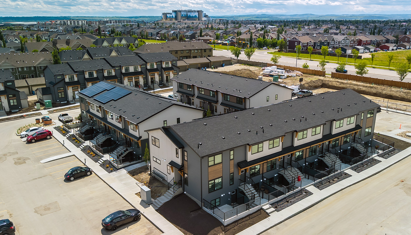 Drone photograph of newly built ZEN Mahogany townhomes with contemporary architecture, solar panels, parking lots, and surrounding residential neighbourhood under a partly cloudy sky.