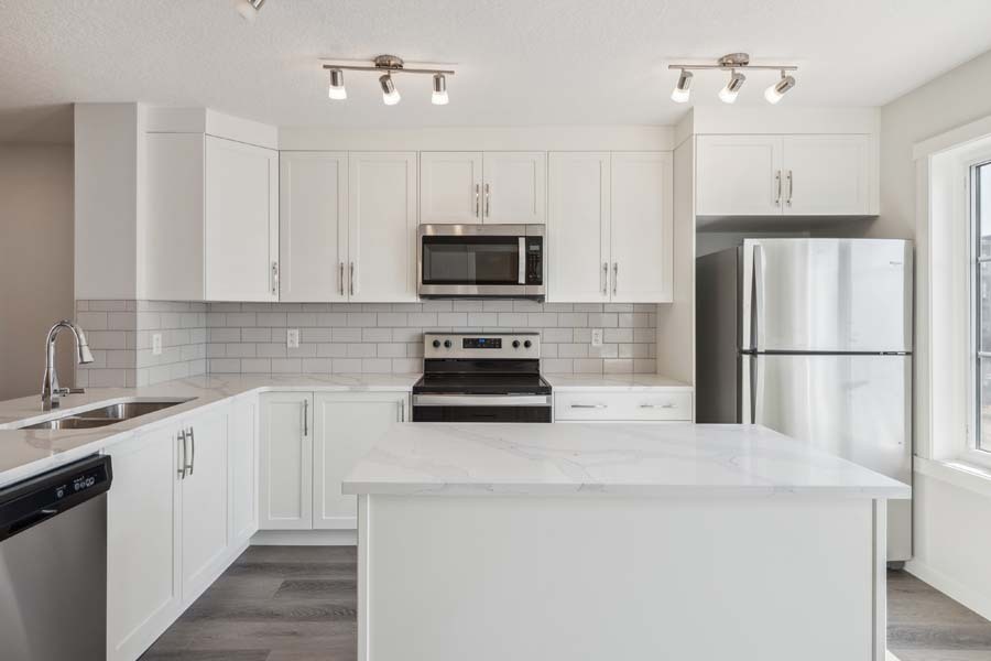 Bright modern kitchen in a Net Zero townhome by Avalon Homes in Calgary featuring quartz island, white cabinetry, and stainless steel appliances