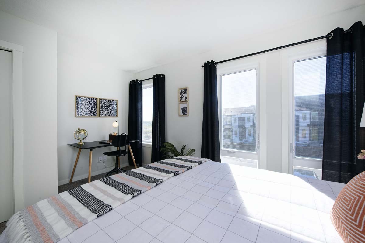 Bright modern bedroom with a desk, black curtains, large windows, and simple decor, perfect for a home office or study space.
