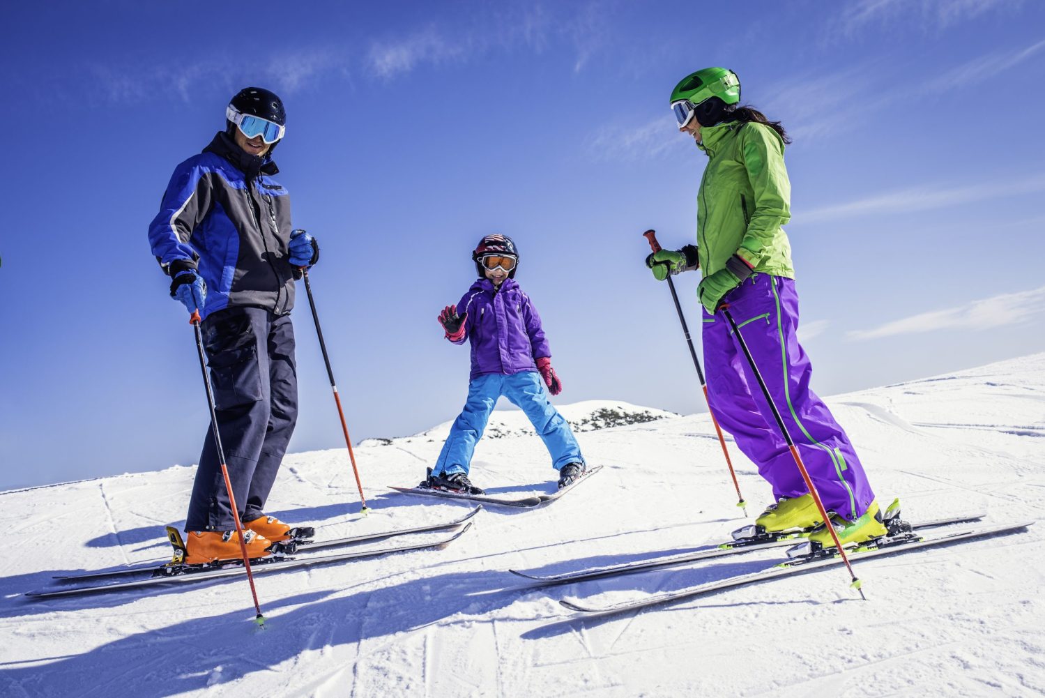 Close up view of a family with one child standing on ski slope.